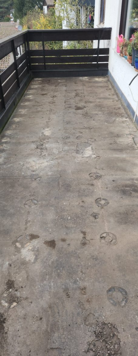 Leere Terrasse mit Holzgeländer und sichtbarem, unbefestigtem Boden.