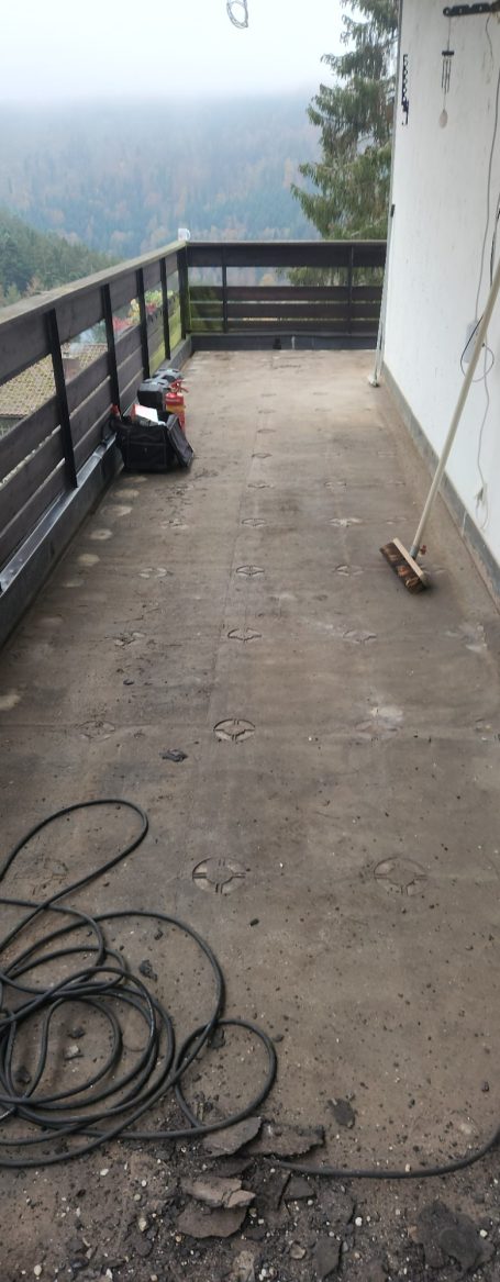 Leere Terrasse mit Holzgeländer und sichtbarem, unbefestigtem Boden.